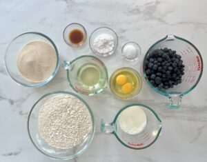 Ingredients needed to make blueberry muffins. Flour, sugar, salt, baking powder, eggs, vegetable oil, milk fresh blueberries